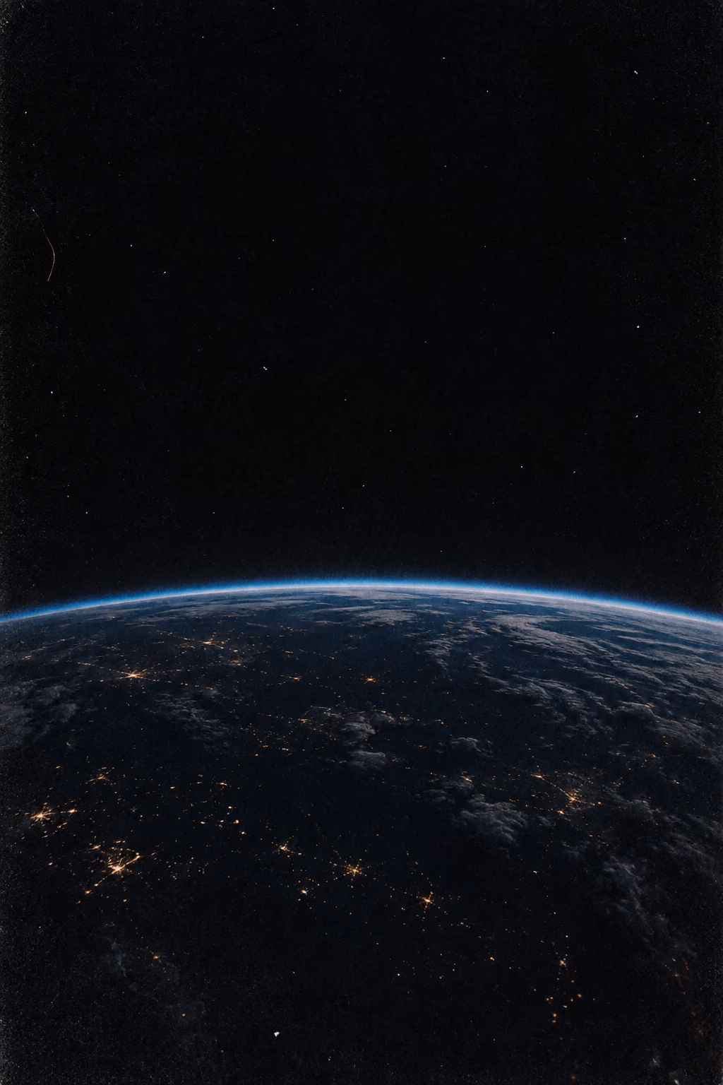 The curve of the Earth at night from orbit: a thin blue rim of atmosphere over scattered amber city lights.